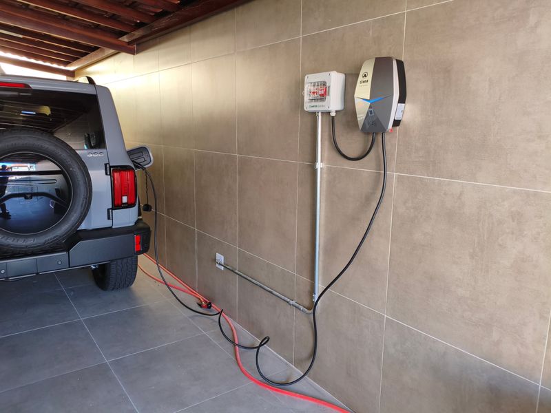 Carregador de carro elétrico instalado na parede da garagem com o veículo conectado, circuito dedicado e caixa de proteção